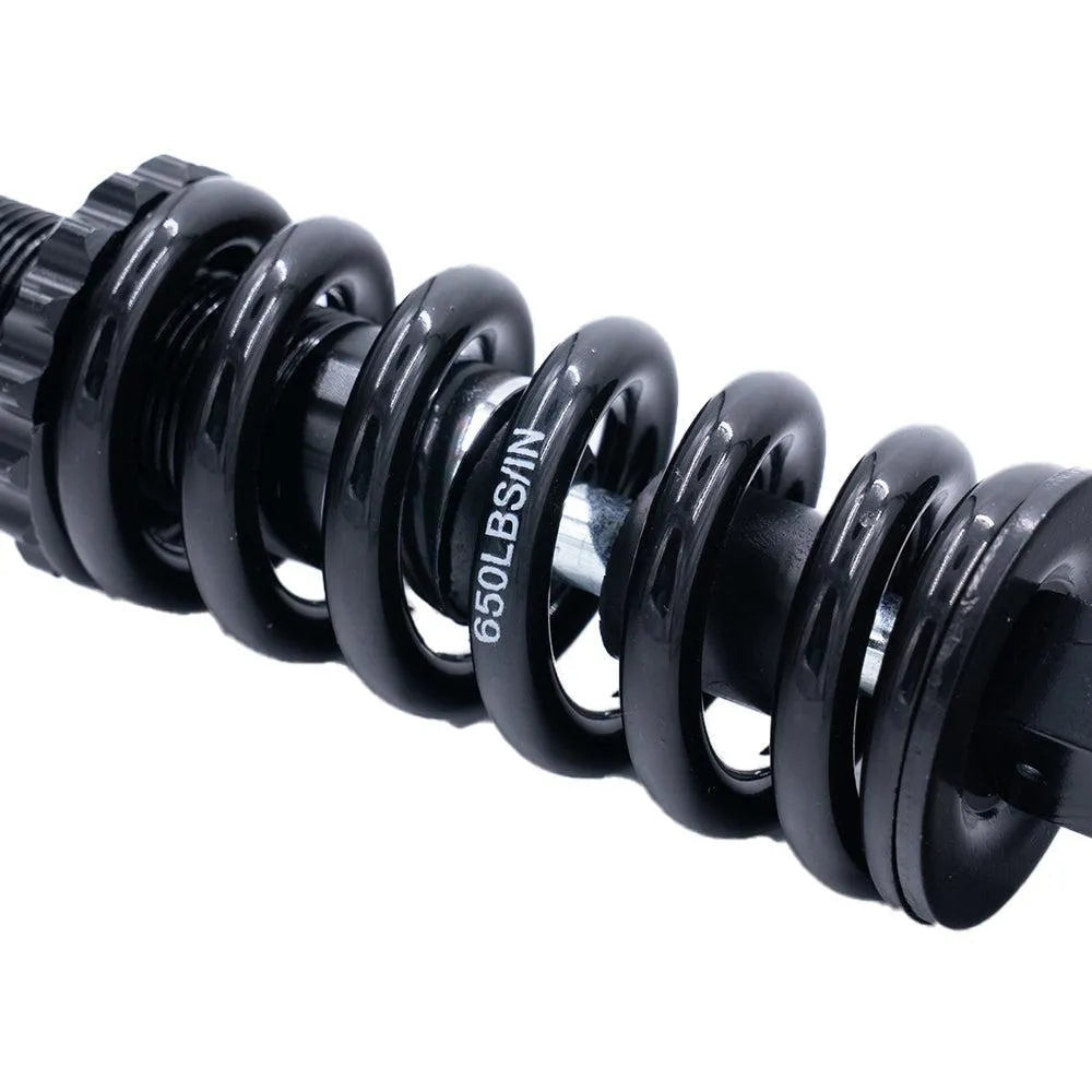 Close-up van de QMWHEEL V20 (PRO) - VERING - ORIGINEEL, een zwarte metalen spiraalveer met de opdruk 650LBS/IN, waarbij de details van de windingen en de structuur goed te zien zijn. Deze originele veer van QMWHEEL dient als vervangingsonderdeel voor fatbikes en is volledig compatibel met het QMWheel V20 Pro-veersysteem.