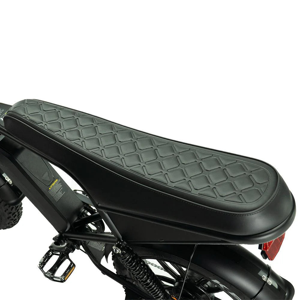 Close-up van een zwart, gewatteerd fietszadel met een ruitjespatroon, gemonteerd op de OUXI FATBIKE V8 PRO (C80 PRO) – MODEL 2026. Het frame, de pedalen en de achtervering van de e-bike zijn gedeeltelijk zichtbaar.