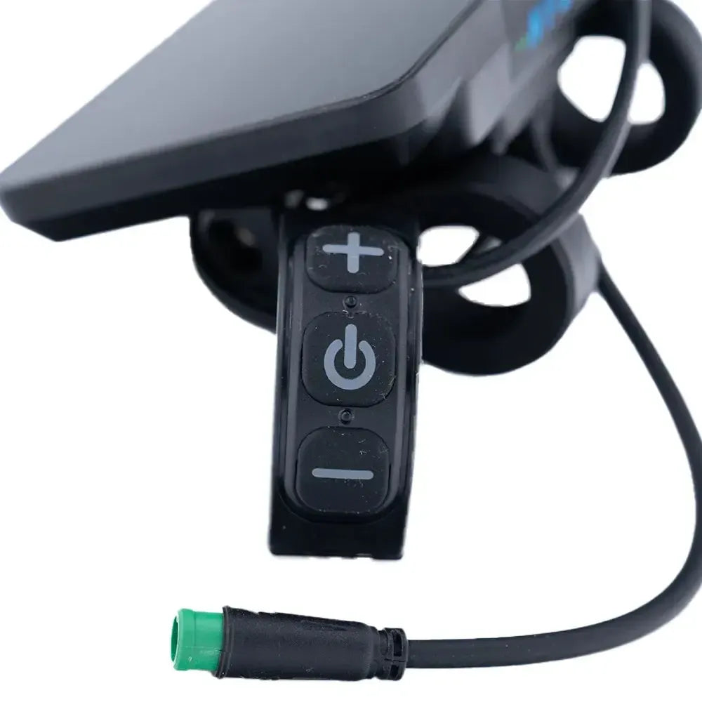 Close-up van een zwarte QMWHEEL FATBIKE S20 (PRO) - NFC - DISPLAY, met drie knoppen met de opschriften ‘plus’, ‘power’ en ‘minus’, stevig bevestigd op een stuur. Op de voorgrond is een zwarte kabel met een groene stekker te zien.