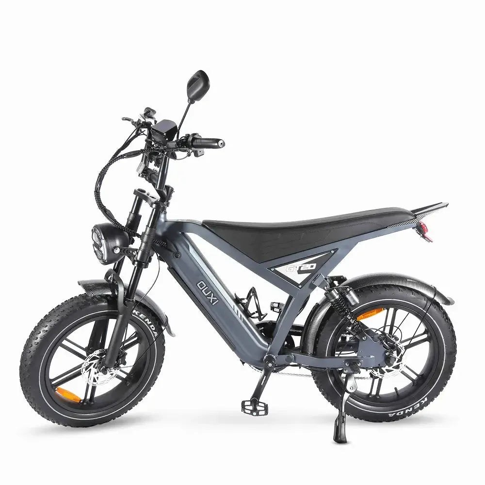 De FATBIKE OUXI GT20 – MODEL 2026 van OUXI heeft een modern ontwerp met dikke banden, een strak grijs frame, een zwart zadel, zijspiegels, een koplamp en een klein achterspatbord. Deze elektrische fatbike, hier vanaf de zijkant afgebeeld op een witte achtergrond, is bovendien uitgerust met hydraulische remmen en een alarm.