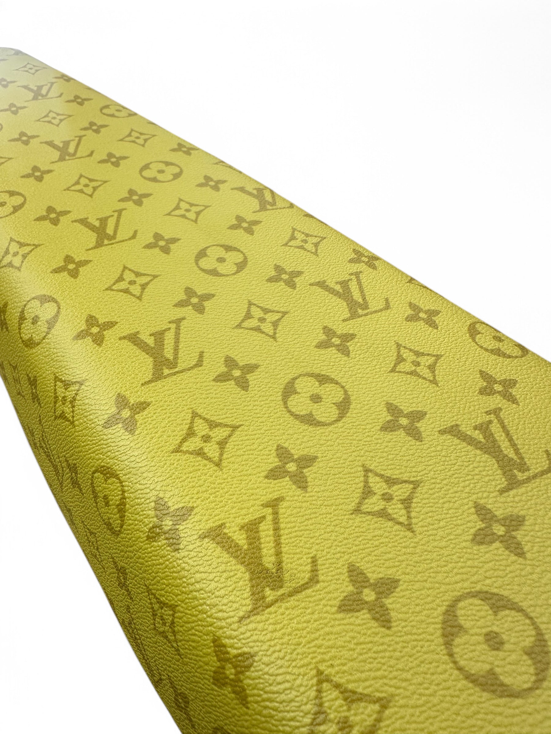 Close-up van een geel, gestructureerd oppervlak met het kenmerkende, op Louis Vuitton geïnspireerde monogram met de initialen LV en bloemmotieven, tegen een witte achtergrond — wat de luxueuze uitstraling en het hoogwaardige comfort oproept die kenmerkend zijn voor de QMWHEEL, OUXI FATBIKE ZADEL CUSTOM V20 - V8 - H9 in diverse kleuren (op maat gemaakt fietszadel).