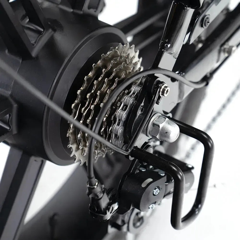 Close-up van de achtercassette, de derailleur en een deel van de ketting van een fiets. De metalen onderdelen zijn gemonteerd op een zwart frame, waardoor de mechanische details die kenmerkend zijn voor een OUXI FATBIKE V8 (C80) – MODEL 2026 goed tot hun recht komen. Dit model is voorzien van hydraulische remmen voor betere remprestaties.