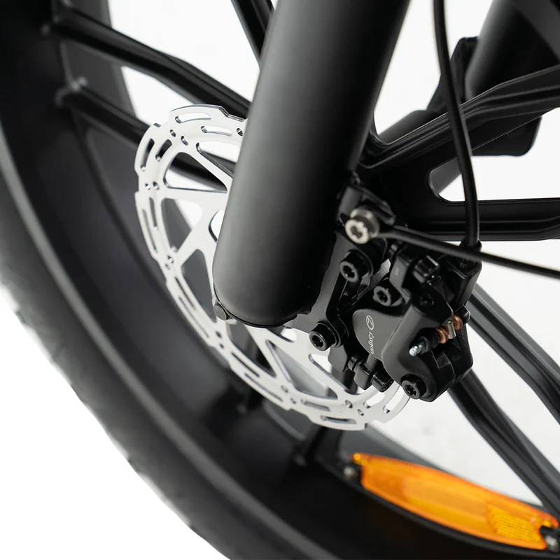 Close-up van een fietswiel van de OUXI FATBIKE V8 (C80) – MODEL 2026, waarbij het hydraulische schijfremsysteem met de remschijf en de remklauw in beeld is, evenals een deel van de zwarte band met een oranje reflector.