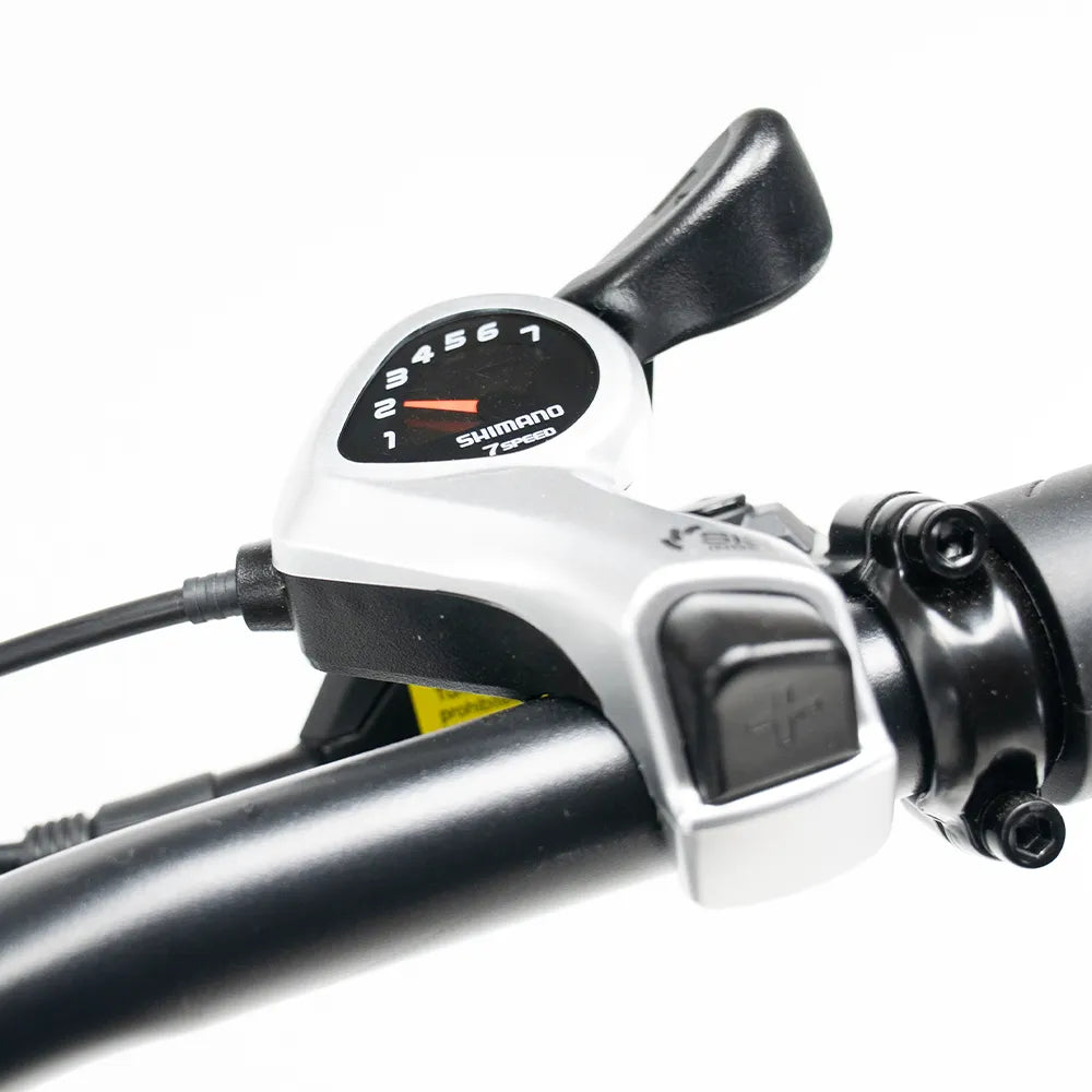 Close-up van een Shimano Tourney-versnellingshendel gemonteerd op het stuur van de OUXI FATBIKE V8 (C80) MAX – DUBBELE ACCU – MODEL 2026, met versnellingsnummers 1 tot en met 6 en een zwarte hendel voor soepel schakelen. De robuuste motor van 250 W en het dubbele accusysteem zorgen ervoor dat elke rit soepel en efficiënt verloopt.