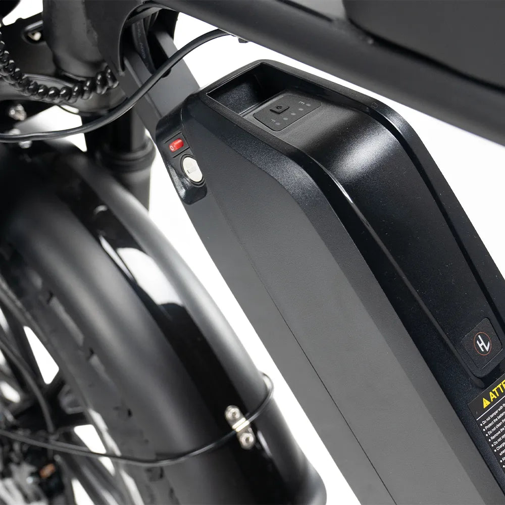 Close-up van een zwarte OUXI FATBIKE V8 (C80) MAX elektrische fietsaccu die op het frame is gemonteerd, met een zichtbare aan/uit-knop en indicatielampjes bij het achterwiel en het spatbord; uitgerust met een motor van 250 W voor betrouwbare prestaties. Deze versie van MODEL 2026 is voorzien van een dubbele accu, een alarm en hydraulische remmen.