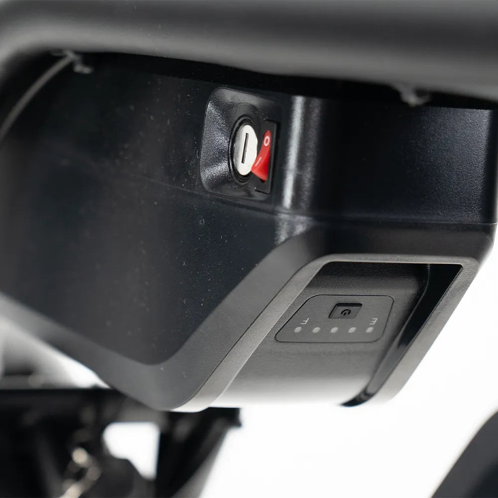 Close-up van een zwart elektronisch apparaat met een sleutelgat, een rode schakelaar, een display met kleine LED-lampjes en een aan/uit-knop – essentiële onderdelen van de OUXI FATBIKE V8 (C80) MAX - DUBBELE ACCU – MODEL 2026 van OUXI. Deze geavanceerde fatbike beschikt over een krachtige motor van 250 W en is uitgerust met hydraulische remmen en een alarmsysteem, evenals ondersteuning voor dubbele accu (dual battery).