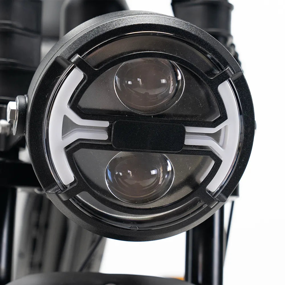Close-up van een ronde motorfietskoplamp met twee lenselementen en een opvallend wit patroon in de zwarte behuizing, dat aansluit bij de gedurfde vormgeving van de OUXI FATBIKE V8 (C80) MAX – DUBBELE ACCU – MODEL 2026, bekend om zijn krachtige functies en moderne ontwerp van OUXI.
