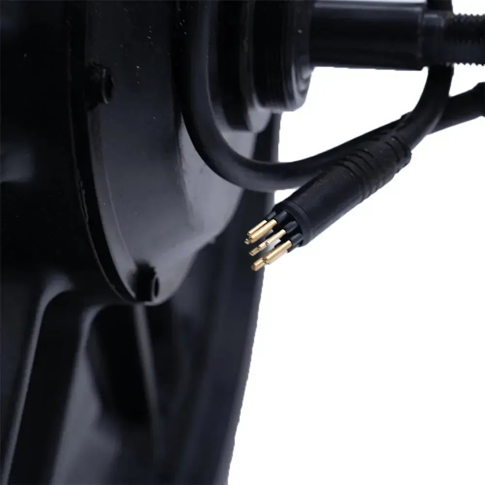 Close-up van een zwarte elektrische connector met blootliggende gouden pinnen, geplaatst naast een rond zwart mechanisch onderdeel — mogelijk de originele fatbike-motor of een vervangend exemplaar, zoals de OUXI C80 MINI - MOTOR van OUXI.