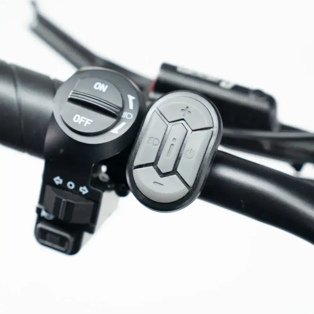 Close-up van het stuur van de OUXI FATBIKE OUXI C80 MINI in lichtblauw (model 2026), met in het bijzonder een zwarte aan/uit-schakelaar met indicatiesymbolen en een compacte ovale controller met meerdere knoppen, die naast elkaar zijn gemonteerd – perfect voor het bedienen van je elektrische fatbike, uitgerust met een krachtige 250W-motor, hydraulische remmen en een alarmsysteem.