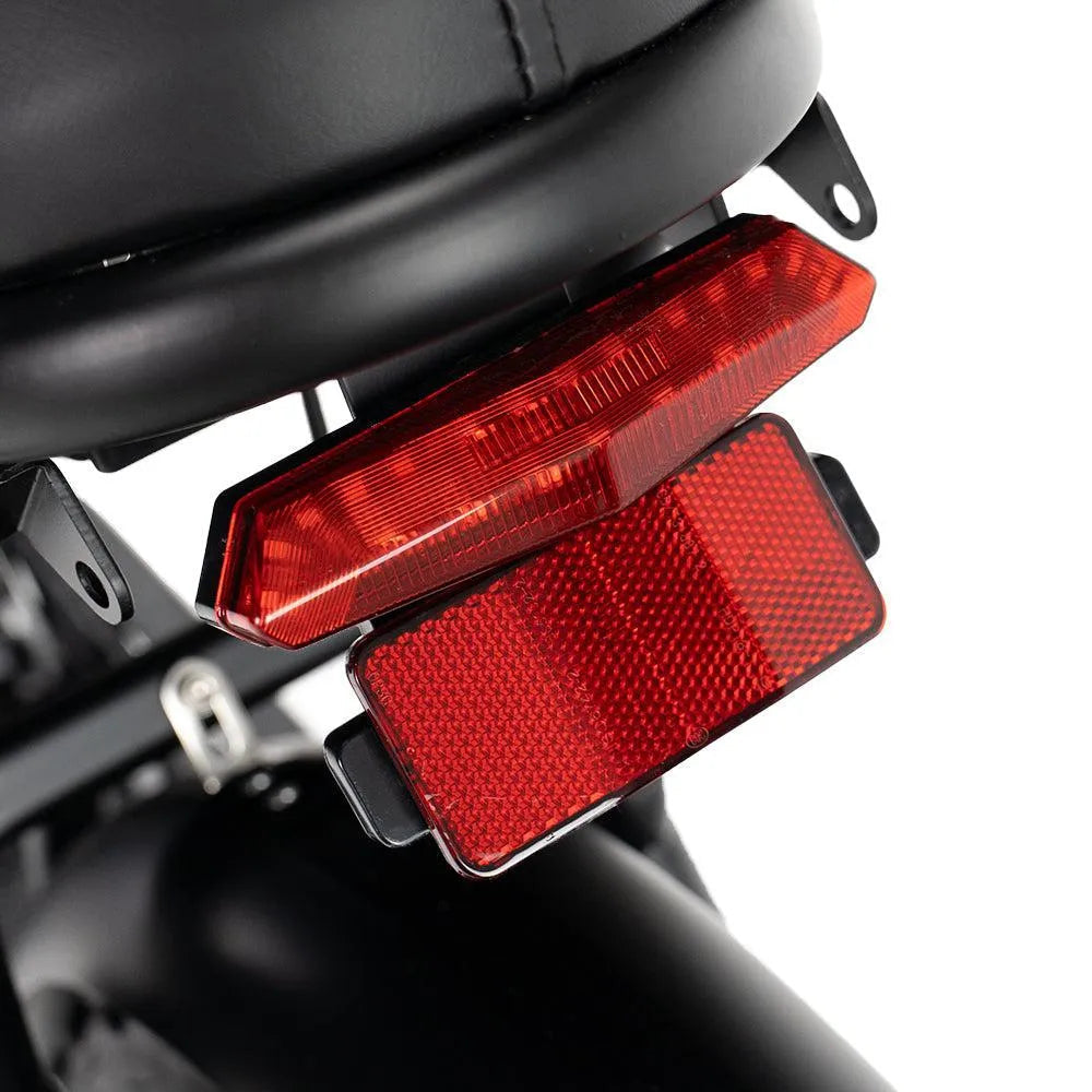 Close-up van een rood achterlicht en een reflector die onder een zwart zadel zijn gemonteerd, waarbij het zwarte spatbord en het frame zichtbaar zijn — wat het hoogwaardige ontwerp benadrukt dat kenmerkend is voor het FATBIKE V8 (C80) MODEL 2026 van OUXI, dat bekend staat om zijn stabiliteit en betrouwbare hydraulische remmen.