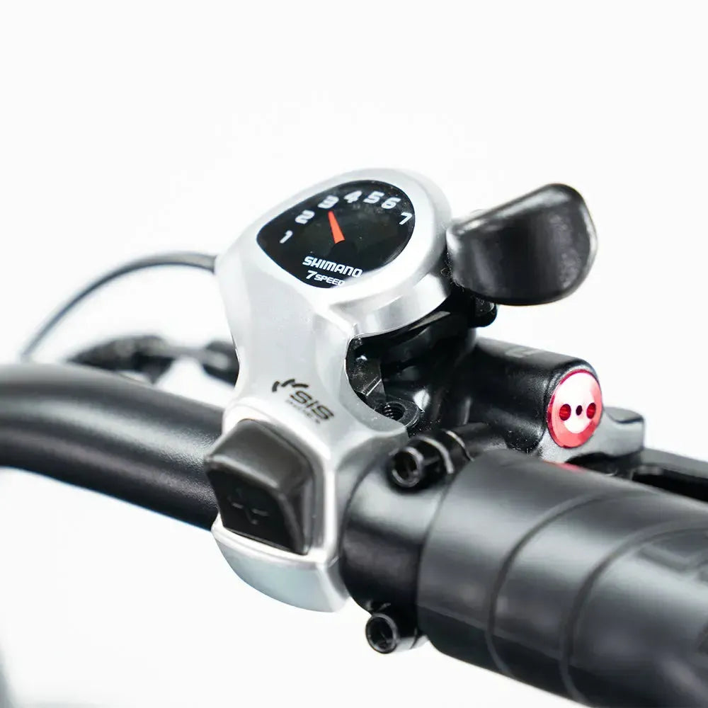 Close-up van een Shimano SIS-versnellingshendel met 7 versnellingen, gemonteerd op het zwarte stuur van de OUXI FATBIKE OUXI C80 MINI in lichtblauw (model 2026), met weergave van de versnellingsnummers en de schakelhendel – ideaal voor nauwkeurig schakelen op je compacte elektrische fatbike met een krachtige 250W-motor, hydraulische remmen en een ingebouwd alarmsysteem.