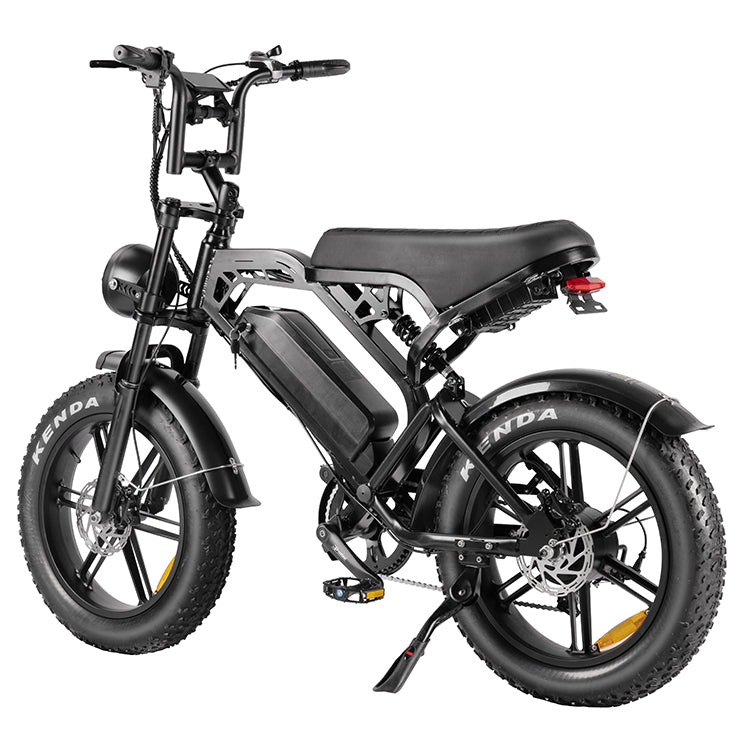 De QMWheel FATBIKE V20 – MODEL 2025 - MECHANIC is een zwarte elektrische fatbike, uitgerust met dikke Kenda-banden, een stevige bagagedrager achterop en een krachtige 48V 15Ah-accu die op het frame is gemonteerd. Dit model beschikt bovendien over schijfremmen en een handige standaard, en is op de afbeelding vanuit een hoek aan de achterzijde te zien.