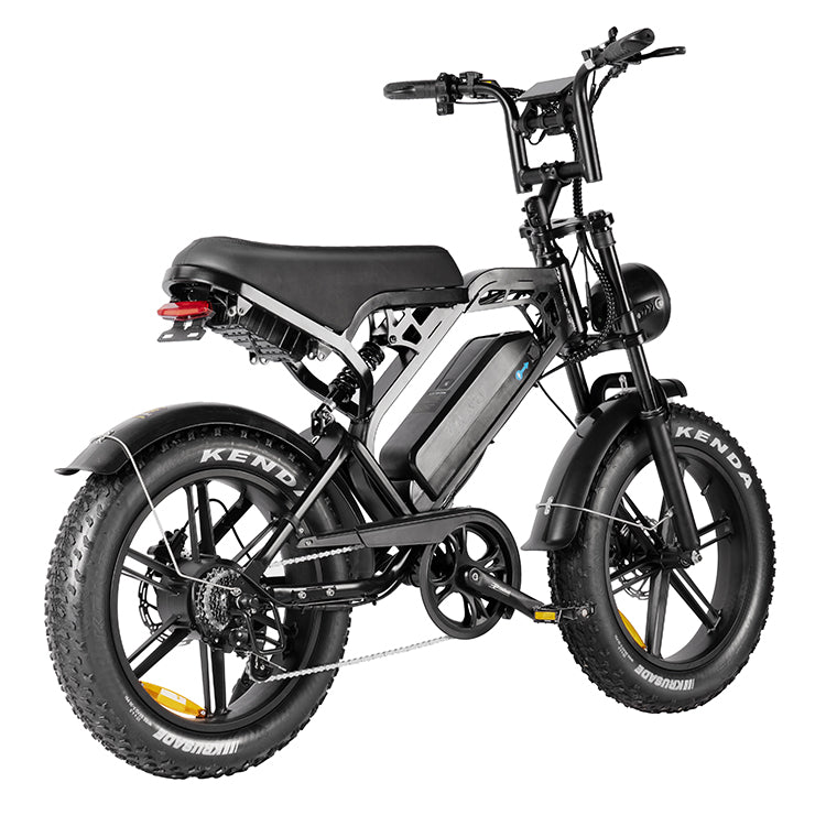 De QMWHEEL FATBIKE V20 – MODEL 2025 - MECHANIC, afgebeeld vanuit een hoek aan de achterzijde tegen een witte achtergrond, is voorzien van een zichtbare, centraal gemonteerde 48V 15Ah-accu, een zwart frame, een bagagedrager achter, een koplamp en een geveerd zadel.
